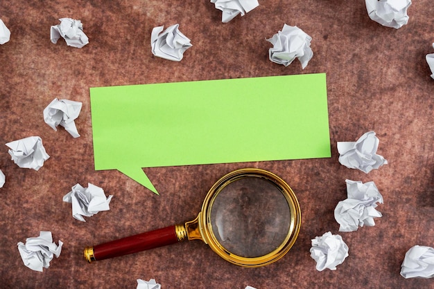 Photo speech bubble made of sheet with magnifying glass surrounded with crumpled papers over wooden background it is showing different thoughts and analyzing strategies