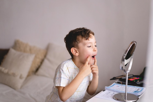 Speech therapy concept Cute little boy pronouncing sound O looking at mirror doing an online Speech therapy lesson through a laptop