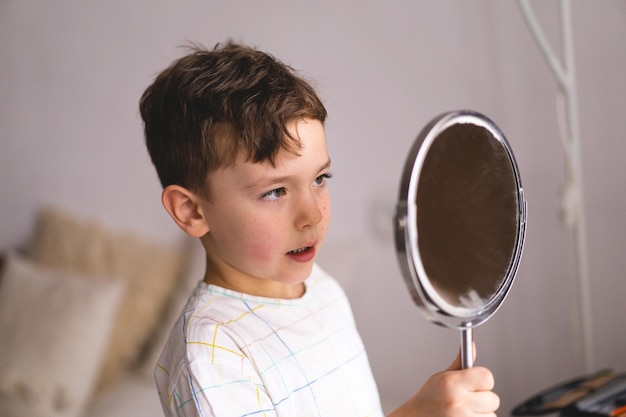 Speech therapy concept Cute little boy pronouncing sound O looking at mirror doing an online Speech therapy lesson through a laptop