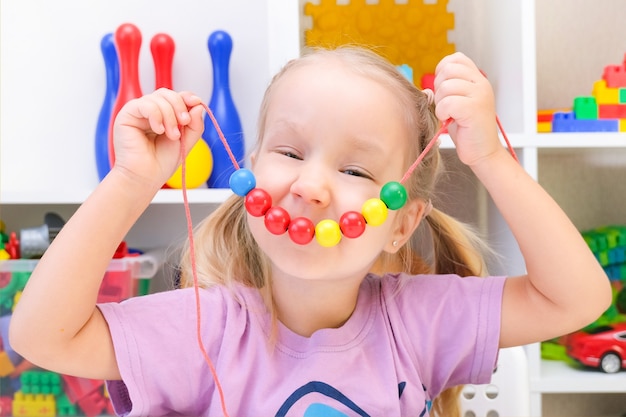 Speech therapy, the development of fine motor skills. Toddler girl is stringing beads on a string.