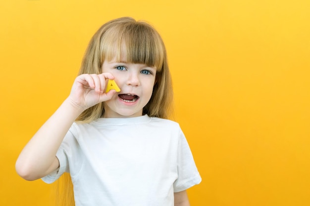 Speech therapy Toddler girl holding the letter A in her hands Classes with a speech therapist Girl on isolated yellow background