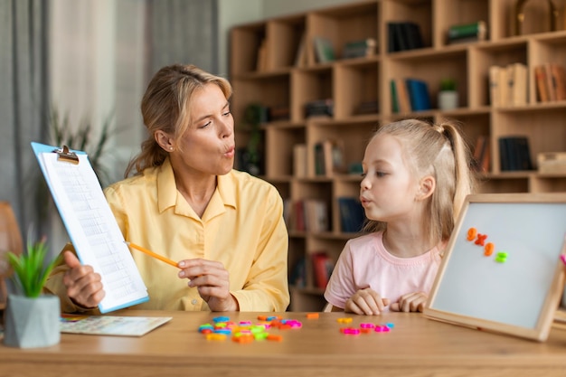 Photo speech training for kids female specialist training with smart little girl teaching her right articulation exercises