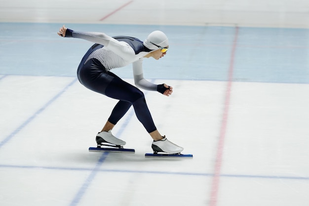 Speed skater bending forwards over ice rink while moving along arena