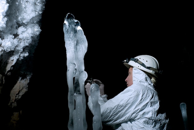 Speleologist takes a sample of the ice structure on the background of a darkness