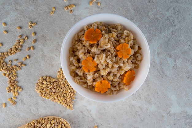 Spelt porridge in a white bowl and decorated with an asterisk carrot, diet food.