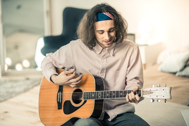 Spending great time. Smiling active young performer in light shirt showing his mastery while playing the guitar