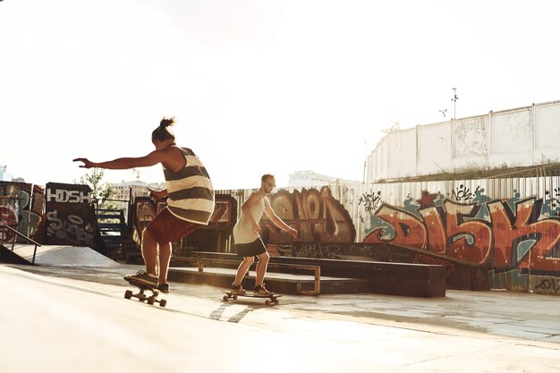 Spending great time with friends. Full length of two young men skateboarding while hanging out at the skate park outdoors