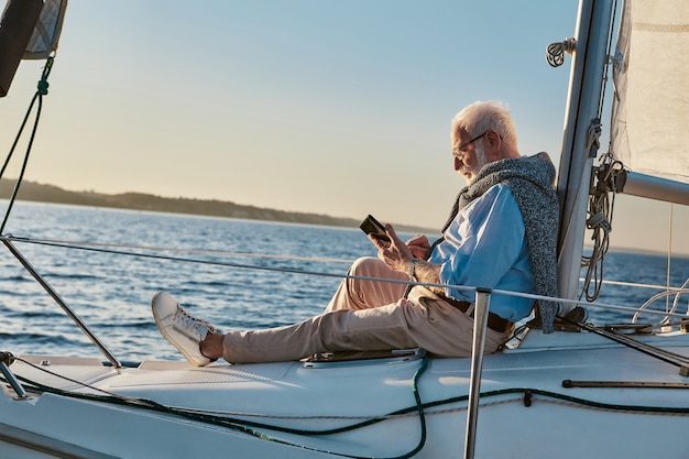 Spending some time alone side view of a relaxed senior man sitting on the side of sailboat or yacht