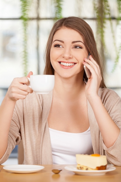 Spending time at the restaurant. Attractive young woman drinking coffee at the restaurant and talking on the phone