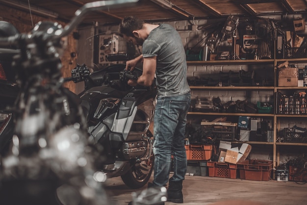 Spending time with bikes. Confident young man repairing motorcycle in repair shop