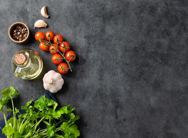 Spices and fresh herbs parsley garlic pepper tomatoes and oil on a dark gray background The concept of delicious and healthy cooking Top view and copy space