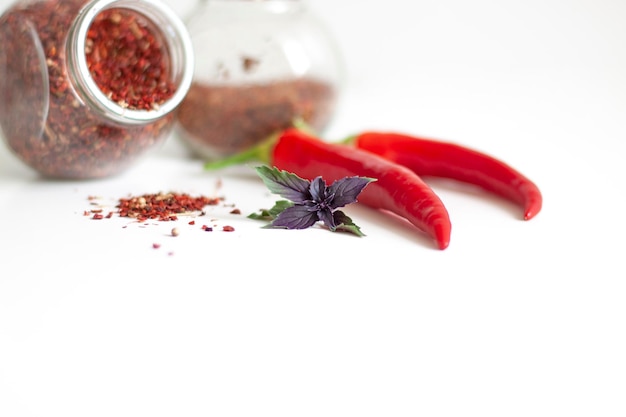 Spices in glass jars and powder pile hot red pepper and basil leaves on white background