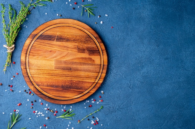 Spices, Herbs and round wooden cutting board on black blue dark concrete backdrop. Top 