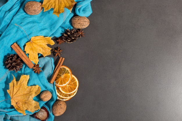 Spices, a scarf, nuts, dry leaves and oranges on a stone table. Autumn mood, a method to keep warm in the cold, copyspace.