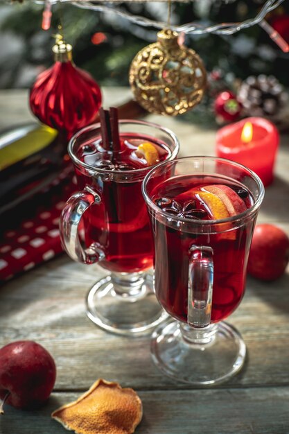 Spicy aromatic hot mulled wine in a couple clear glasses on a wooden table with festive accessories. Concept of a cozy holiday atmosphere, New Year and Christmas mood