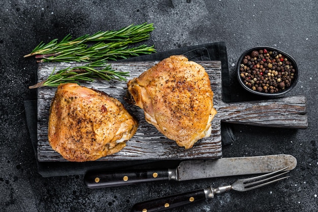 Spicy Bbq grilled chicken thighs on a wooden board with rosemary. Black background. Top View.