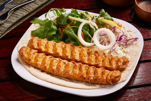 Spicy bbq lamb kabab with salad lemon and bread served in dish isolated on table side view of middle east food