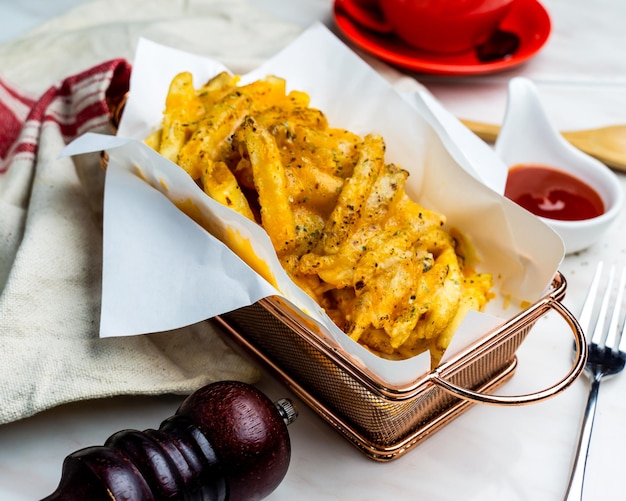 Spicy cheese baked fries served in bucket with ketchup isolated on napkin side view of fastfood on table