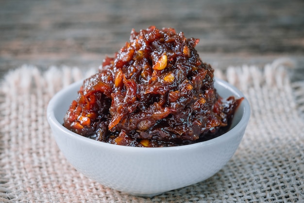 Spicy chili paste in white ceramic container on wooden table