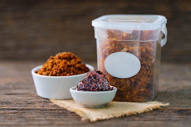 Spicy chili paste in white ceramic and plastic containers on wooden table