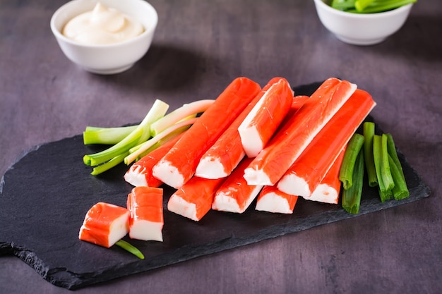 Spicy crab sticks and green onions on a stone board and sauce in a bowl on the table