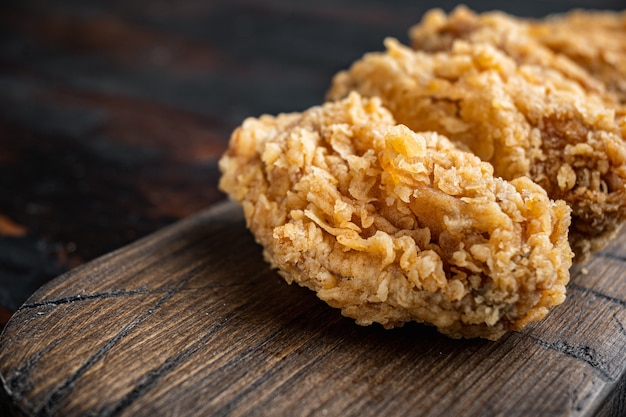 Spicy deep fried breaded chicken wings cuts on dark wooden table.