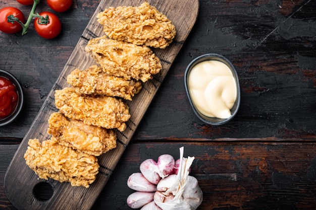 Spicy deep fried breaded chicken wings cuts on old dark wooden table, top view.