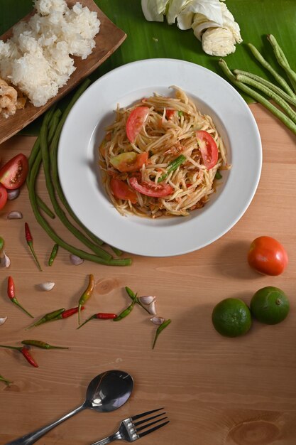 Spicy green papaya salad in white plate on wooden table.