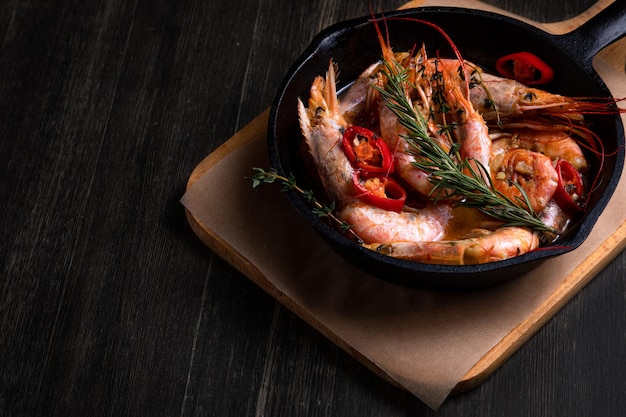 Spicy langoustines with pepper and rosemary in a frying pan served with a glass of wine