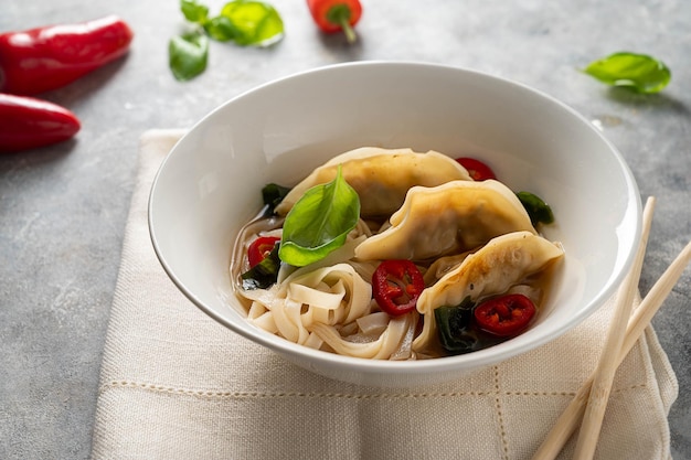 Spicy miso soup with dumplings and rice noodles in white bowl