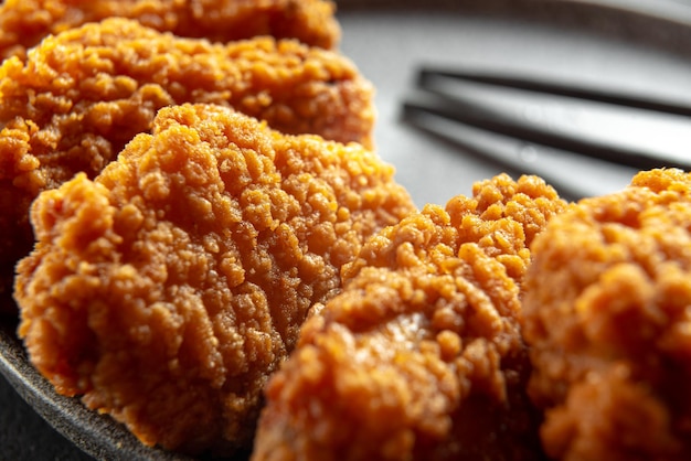 Spicy pieces of chicken fillet in crispy breading on a black plate on a dark background stone or con