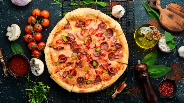 Spicy pizza with sausages and chili peppers On a black stone background Free space for text