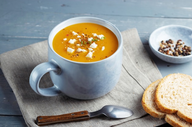 Spicy pumpkin and sweet potatoes soup in big ceramic mug garnished with feta cheese.