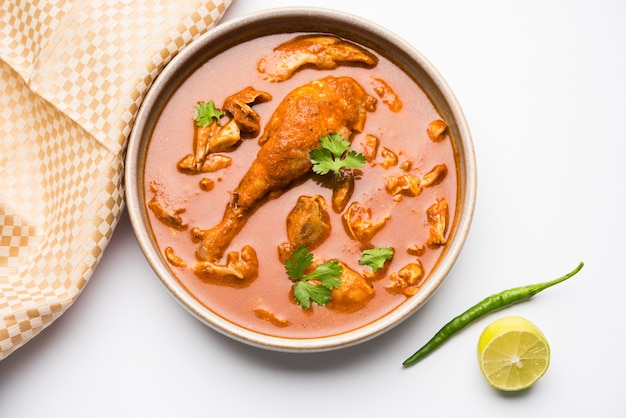 Spicy Reddish Chicken Curry or Masala, with prominent Leg Piece, served in a bowl or Kadhai over colourful or wooden background. selective focus.