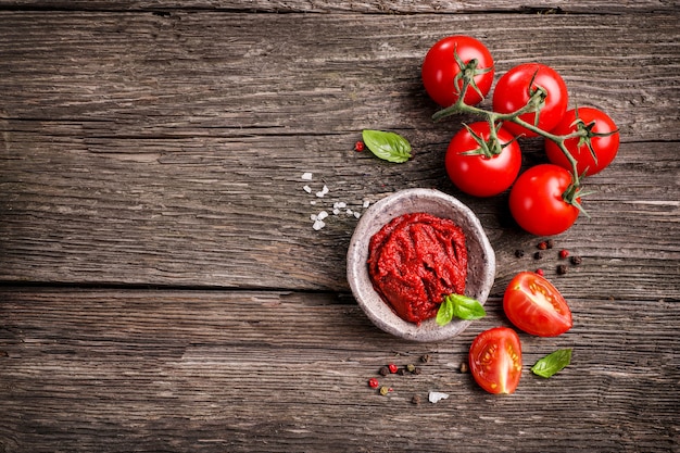 Spicy rich tomato sauce in small bowl with red tomatoes and seasonings on wooden