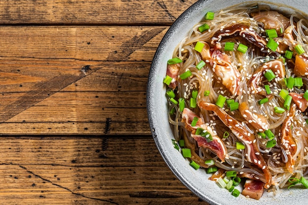 Spicy salad with pork pig ears glass noodles sesame seeds and green onions Wooden background Top view Copy space