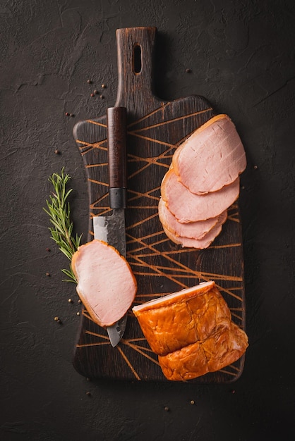 Spicy smoked ham with rosemary and kitchen knife on a black stone table