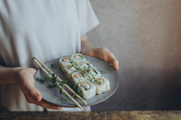 Spicy sushi with fried salmon in hands on a gray plate decorated with microgreens