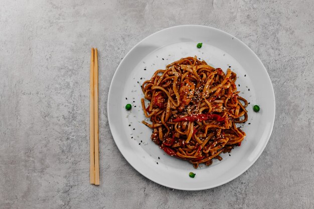 Spicy udon with chicken on a white plate on a gray background.Top view