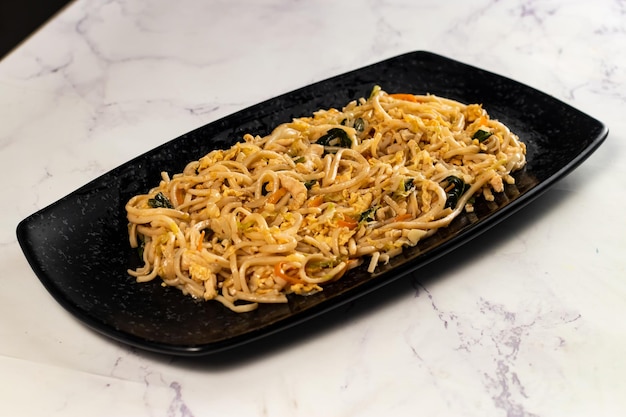 Spicy vegetable chow mein in a black tray isolated on marble background top view of chinese food