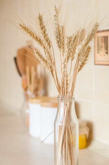 Spikelets close-up on the background of a jar for cereals with wooden lids, wooden cutlery and dried flowers and spikelets in a bottle on the kitchen table, scandinavian style Selective focus