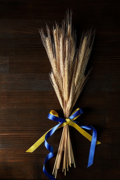 Spikelets with Ukrainian flag colors ribbons on wooden background