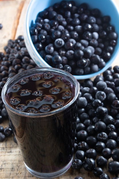 Spilled white bowl full with frozen aronia berries on table with glass of chokeberry juice