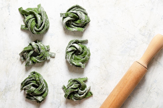 Spinach fettuccine with a wooden rolling pin on a light background