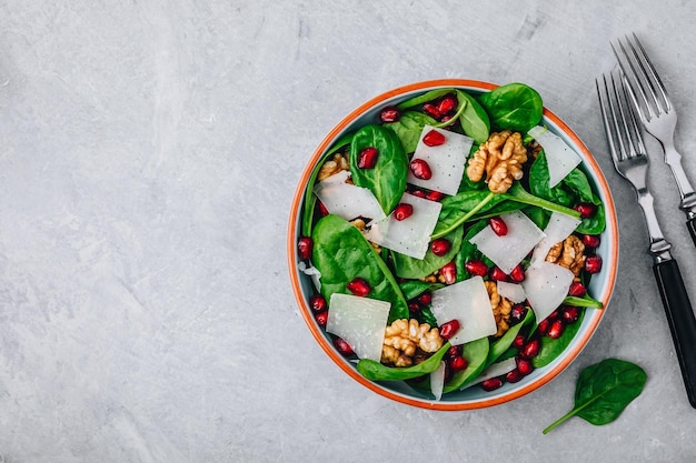 Spinach salad bowl with pomegranate seeds walnuts and cheese slices Top view