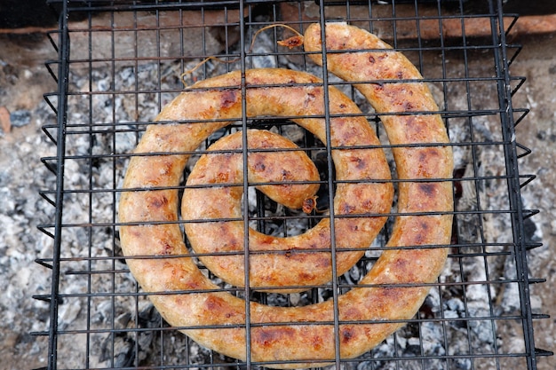 Spiral of homemade sausage is grilled on a charcoal grill