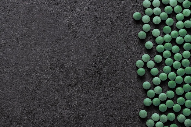 Spirulina pills on black background. Green tablets superfood. Flat lay, top view, copy space