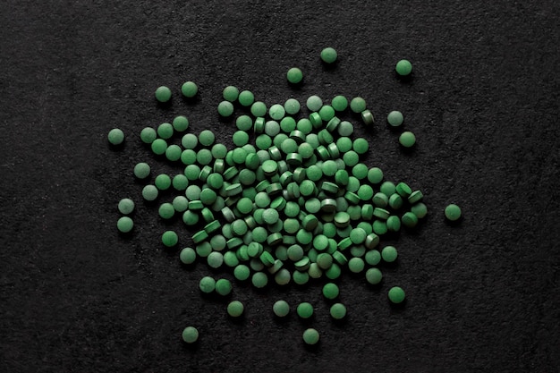 Spirulina pills on black background, top view