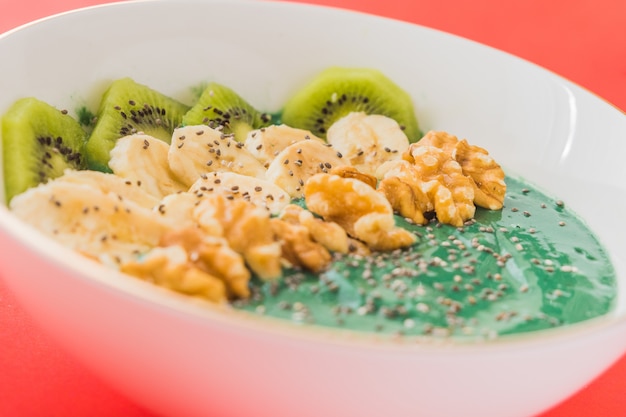 Spirulina smoothie bowl with banana, walnuts, kiwi and chia seeds on red