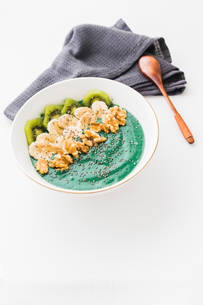 Spirulina smoothie bowl with banana, walnuts, kiwi and chia seeds on white background